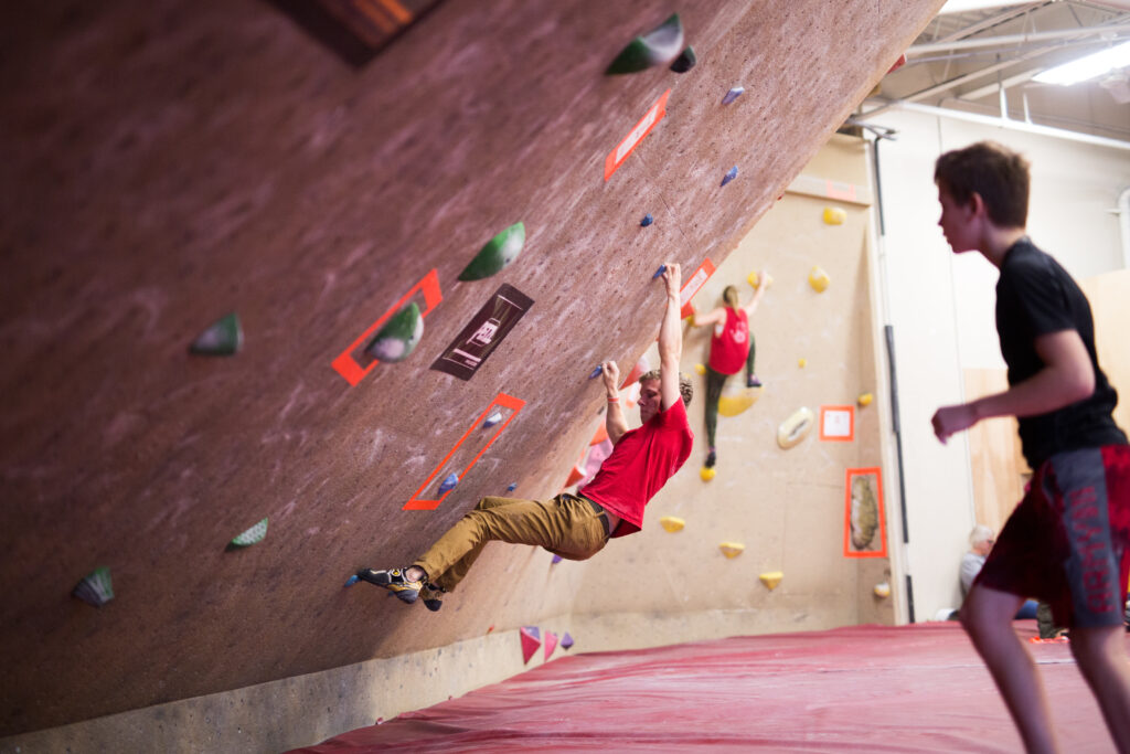 man climbing boulder problem while friend watches.